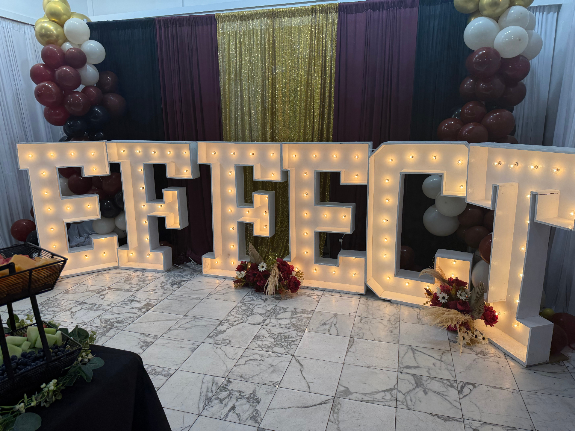 Illuminated marquee letters spelling EFFECT with burgundy and gold draping and balloon garlands at the launch event